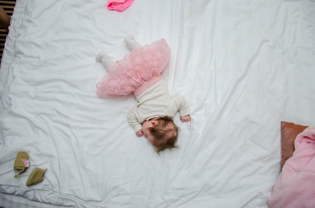 Bábätko v ružovej sukni ležiace na posteli.jpg