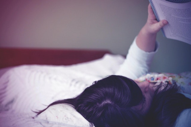 Čiernovlasá žena, ktorá číta knihu v posteli.jpg
